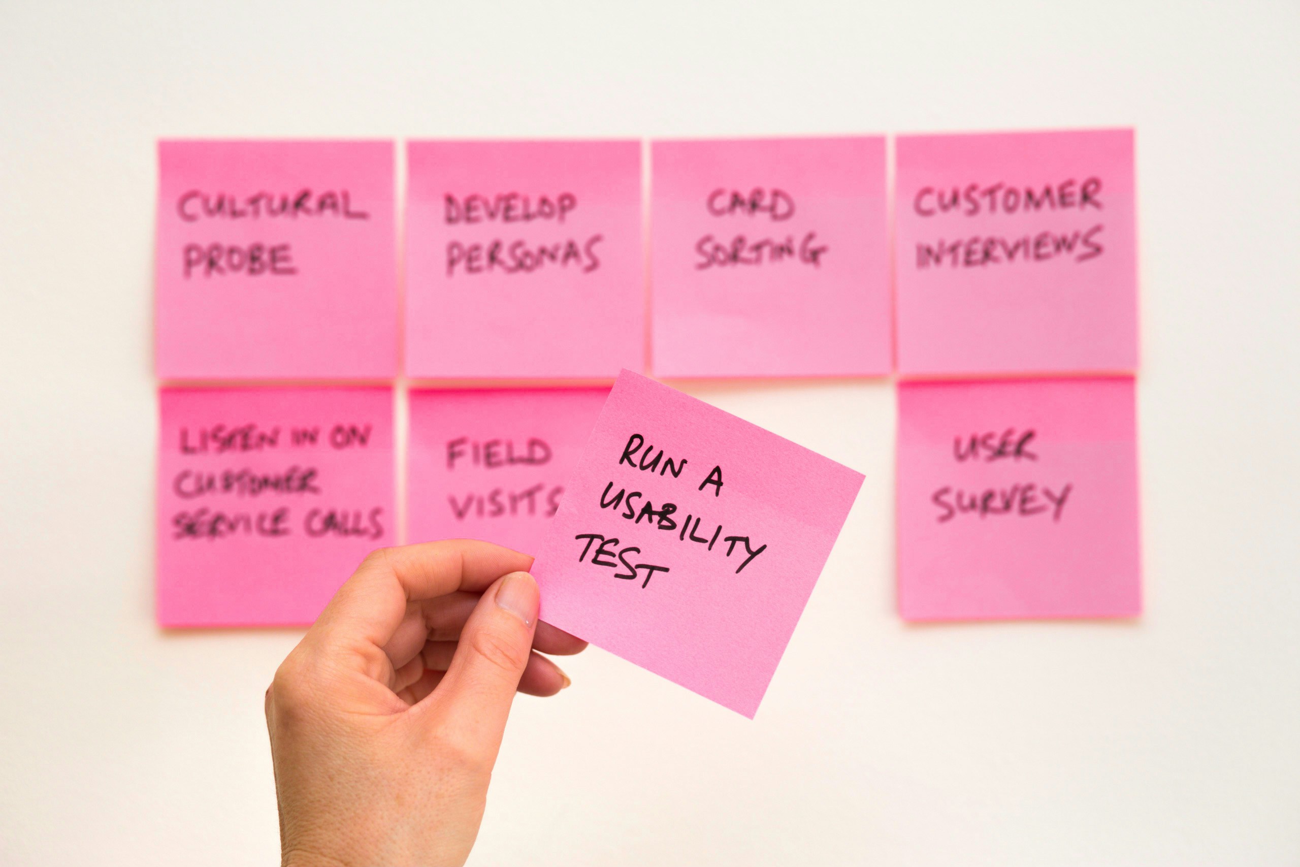 Eight post-its with user research methods, a hand is shown holding the post-it with run a usabiliyt test written on it